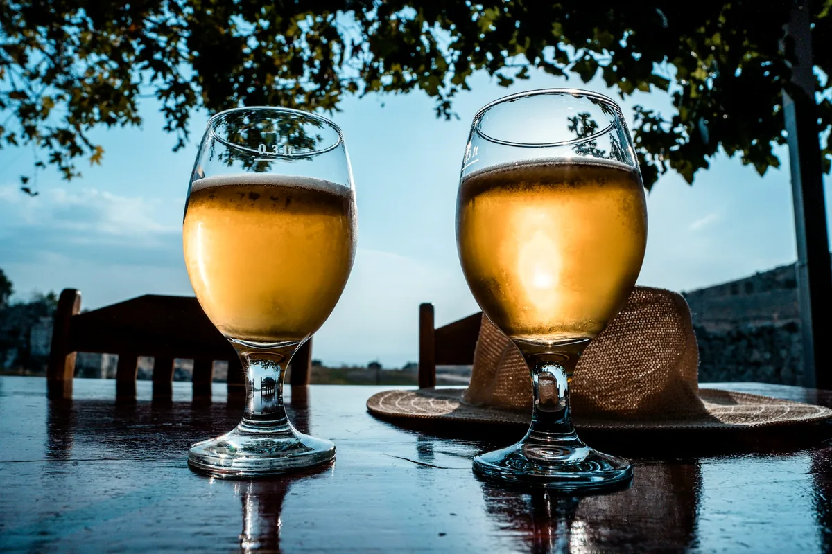 Two stemmed glasses of pale beer on an outdoor table