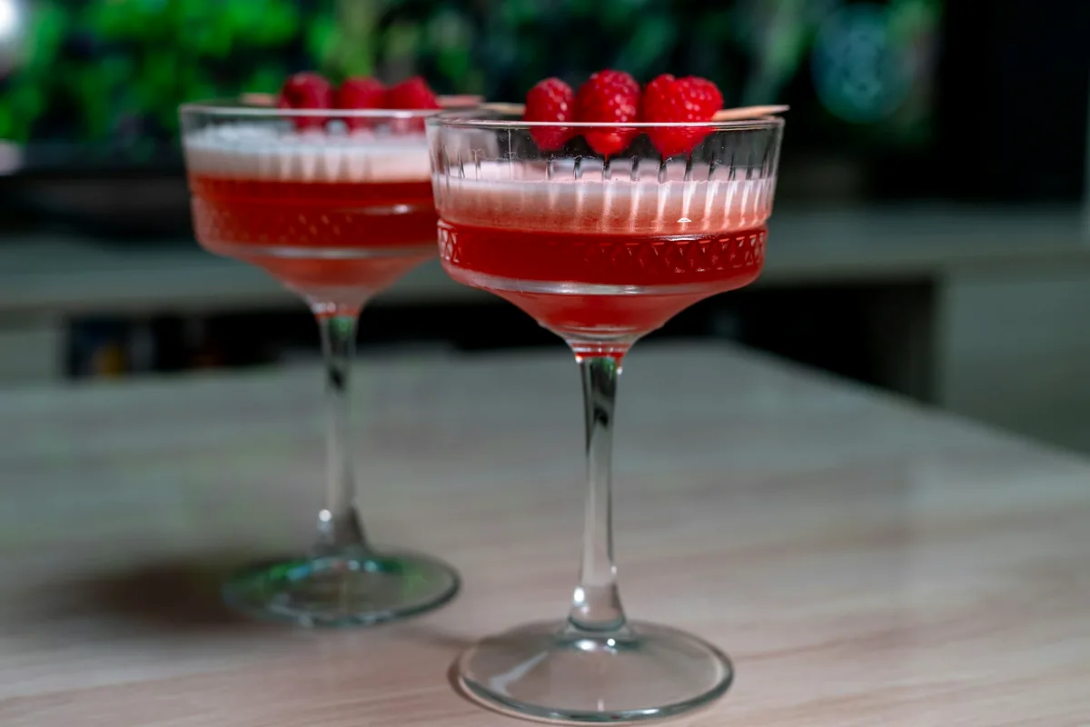 Two deep pink cocktails topped with fresh raspberries on a table
