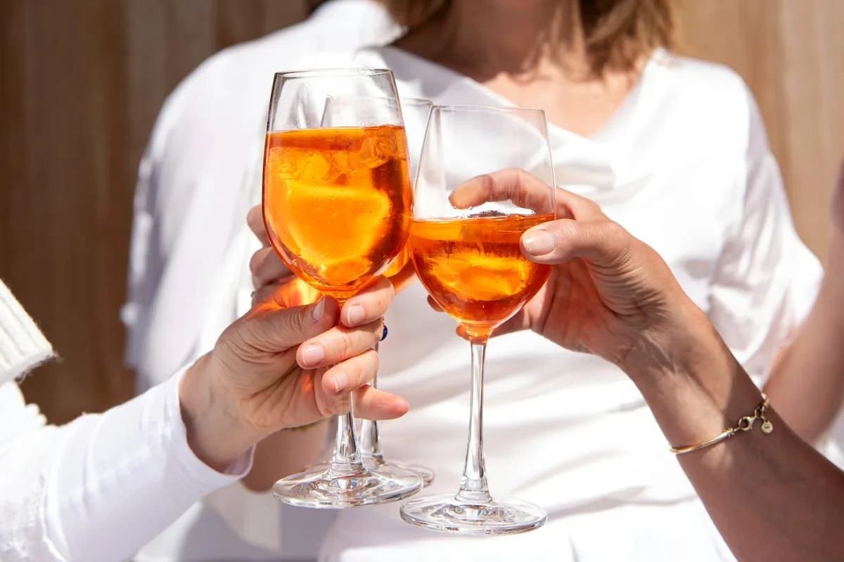 Two hands bringing together two glasses of orange spritz