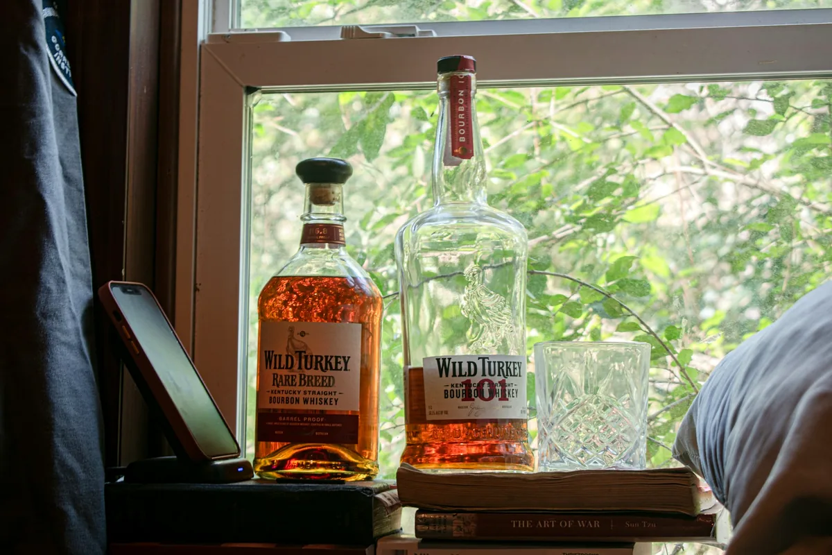 A bottle of whiskey standing on a sill beside a window