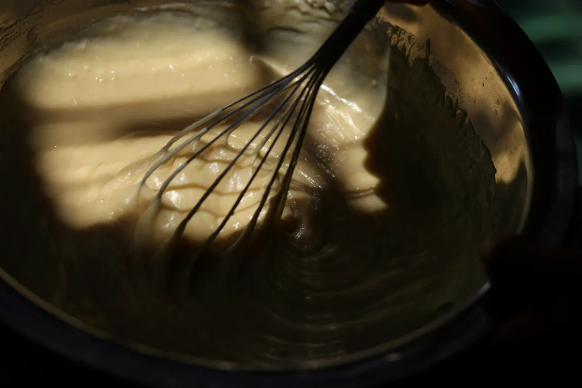 A whisk beating a pale mixture in a bowl